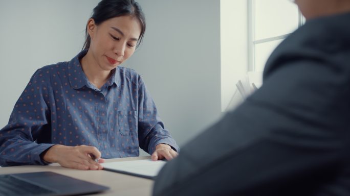 年轻的亚洲女商人在办公室签署纸质合同。