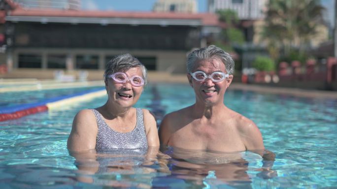 周末早上，亚裔中国老年夫妇在游泳池里看着镜头微笑
