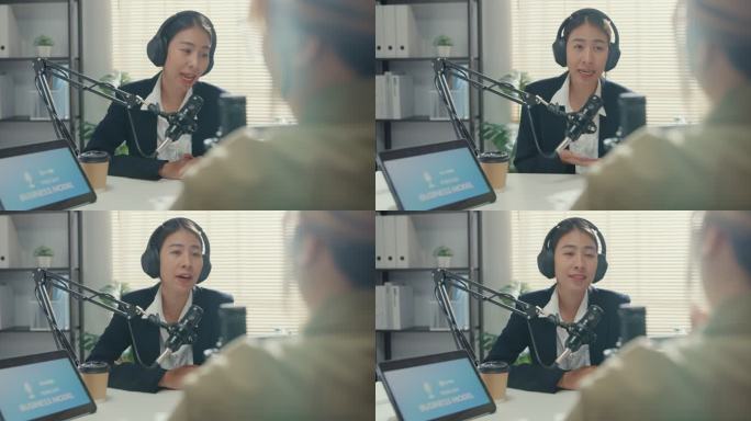 年轻的亚洲女商人采访名人嘉宾内容谈话，并在工作室办公室用笔记本电脑播放播客。
