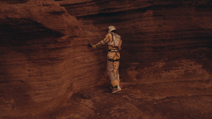 火星上的孤独。女宇航员探索铁锈色的洞穴和岩石。接触石墙