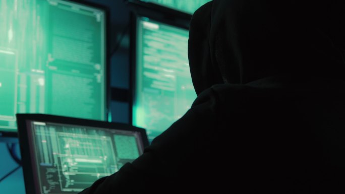 一名黑客程序员穿着连帽衫和黑色黑客面具来隐藏身份，并使用计算机进行黑客攻击，《黑暗互联网的概念》