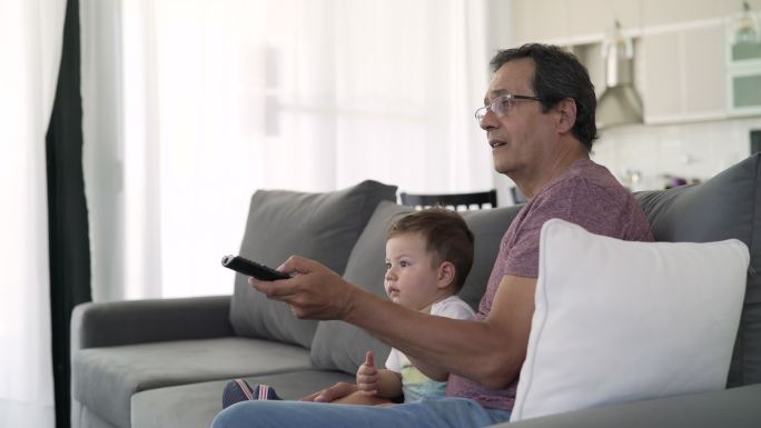 祖父和孙子坐在沙发上换电视频道