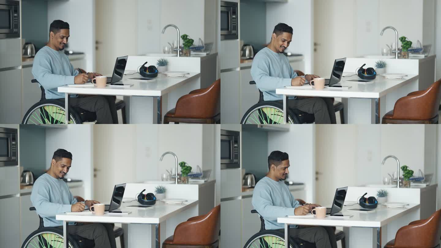 坐在轮椅上的亚裔印度男子坐在餐厅里，用笔记本电脑和书写笔记进行电子学习