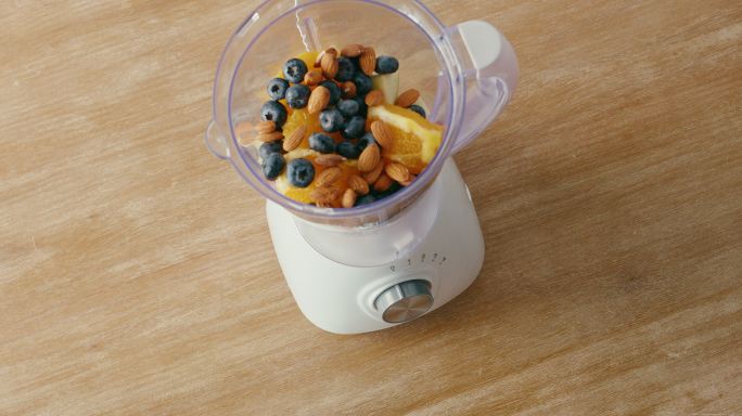 定期将冰沙配料添加到厨房台面上的搅拌器中。草莓、香蕉、苹果、橙子、黑莓、坚果、酸奶、糖浆和许多营养食