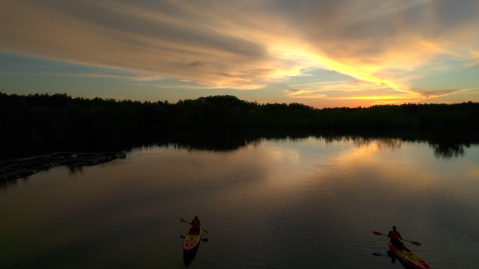 日落景象旅游者或研究人员在淡水河湖划独木舟，发现和探索泰国蓬雅省热带植物园的自然风光