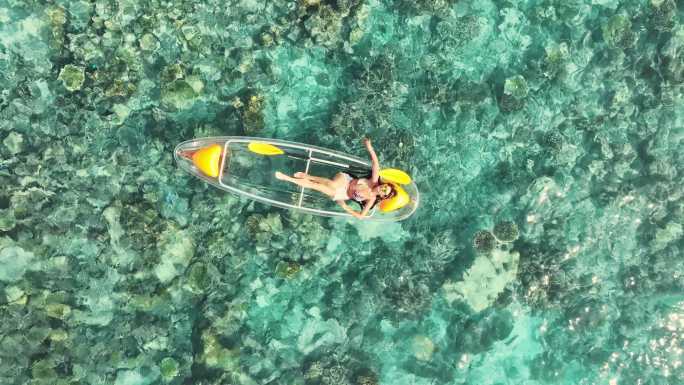 在海洋礁石上乘坐玻璃底船的女子皮划艇鸟瞰图