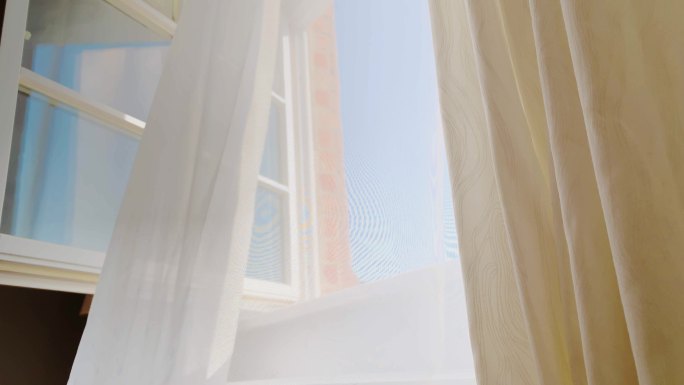 透明的窗帘在夏天的风中在敞开的窗户上飘动