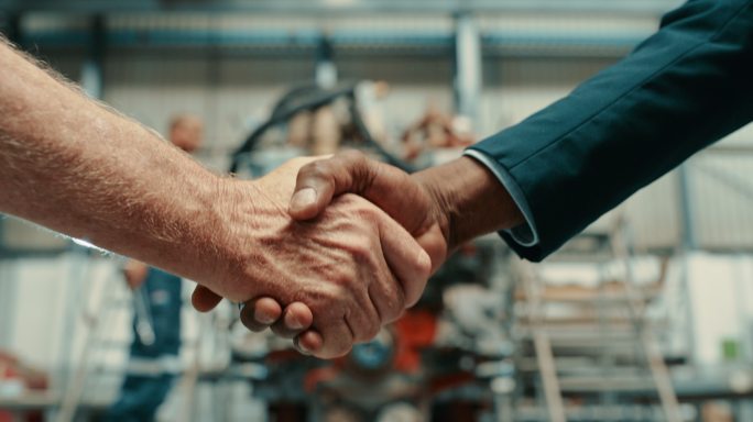 老板雇佣、欢迎或祝贺技工在工厂取得的成就。两名男子在工业设施中握手。工程师和商人在车间握手并达成协议