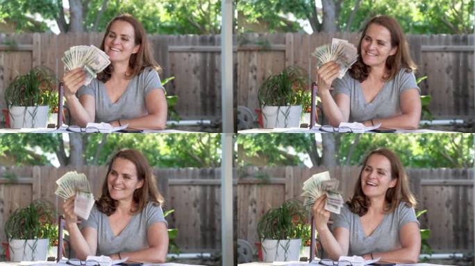 微笑着的成熟女人拿着一把美元坐在后院