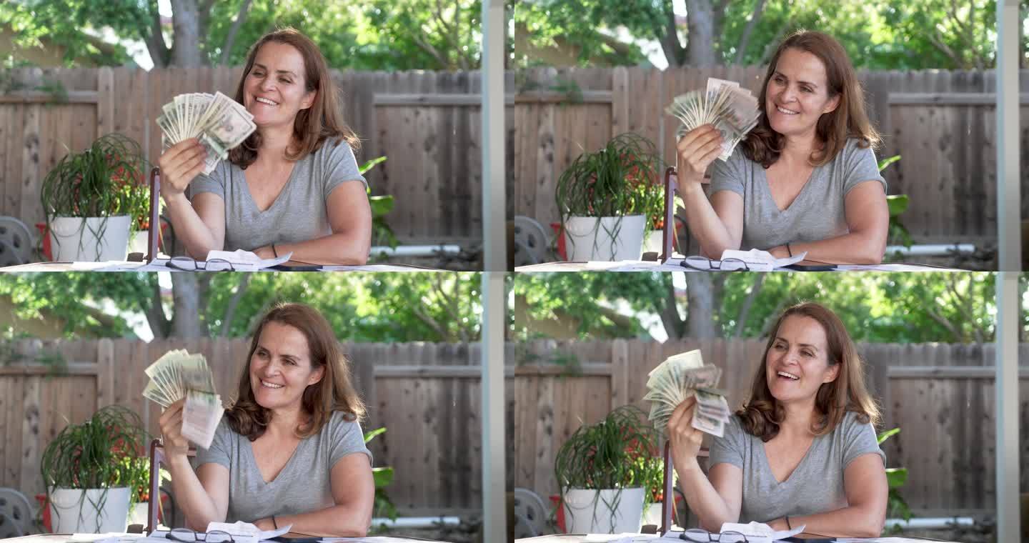 微笑着的成熟女人拿着一把美元坐在后院