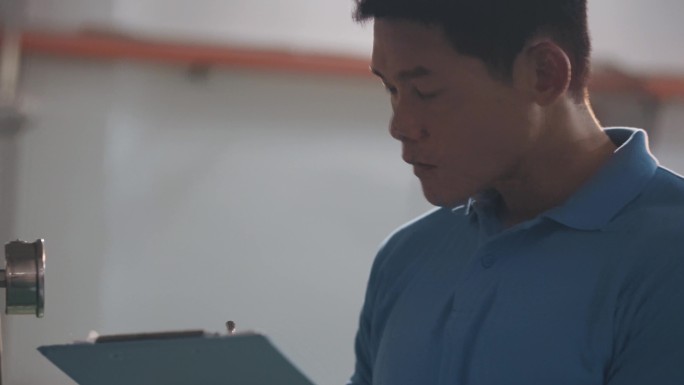 亚裔中国技术人员维护工程师记录水箱中的仪表读数，灌装厂日常质量控制，在剪贴板上书写