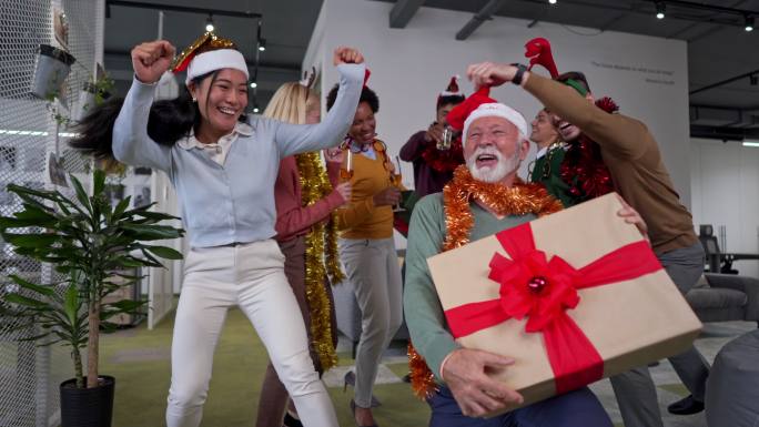 在高级男性首席执行官的带领下，一群多种族同事在办公室的圣诞派对上跳舞