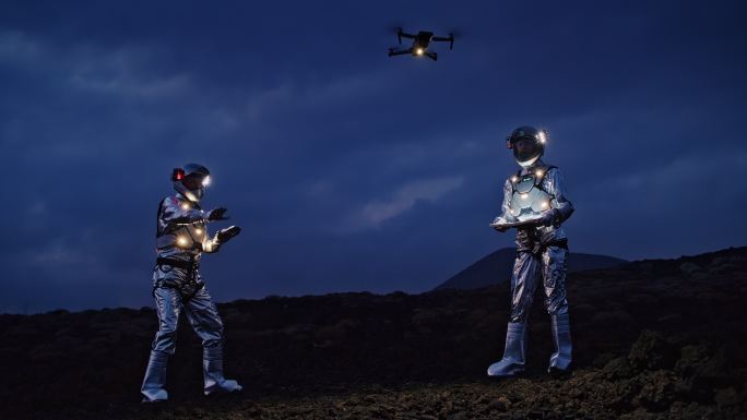 自拍出这个世界。宇航员穿着未来派的照明套装摆姿势。无人机在他们上方飞行