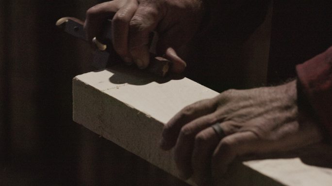 一名白人男性木匠在车间用刻痕规刻划一块木头的手的特写镜头