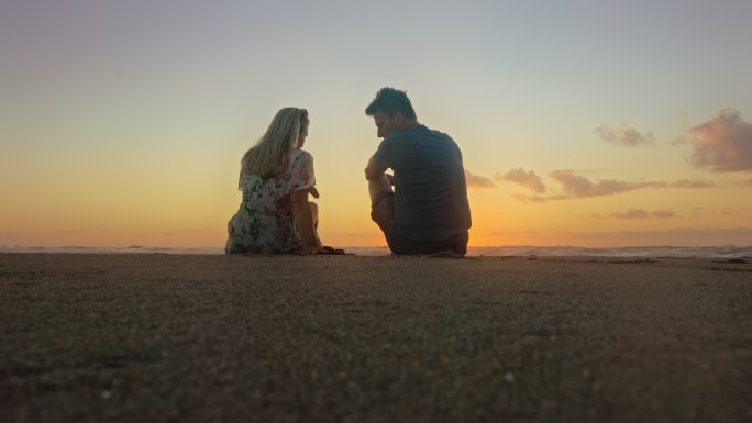 日落时分，一对情侣坐在海滩上，意大利。