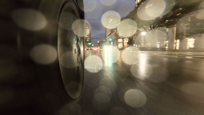 在雨夜驾车穿过城市。汽车车轮特写。