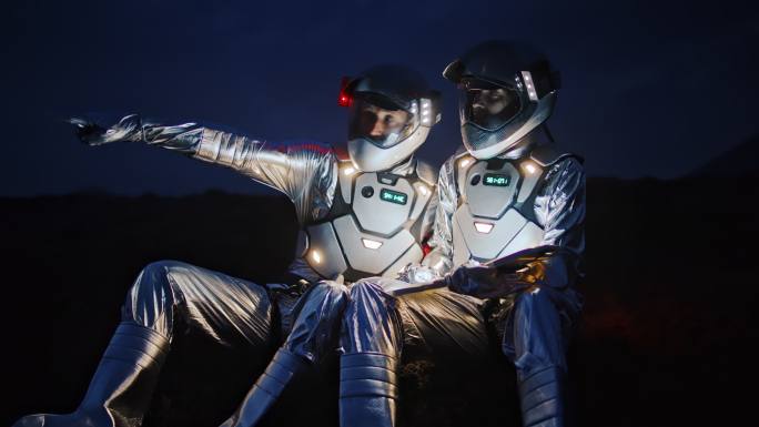 穿着未来主义套装的宇航员在新行星上寻找一条带照明平板的路线。坐在荒凉的海岸上
