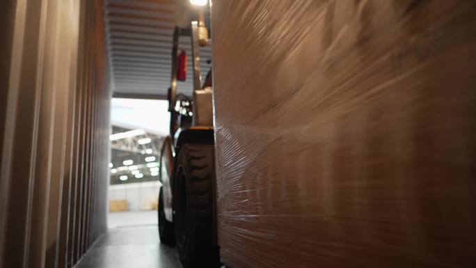 亚洲电动叉车操作员驾驶并提升装有纸箱货物的托盘，从卡车上的集装箱中取出，存放在储藏室中。在配送中心或