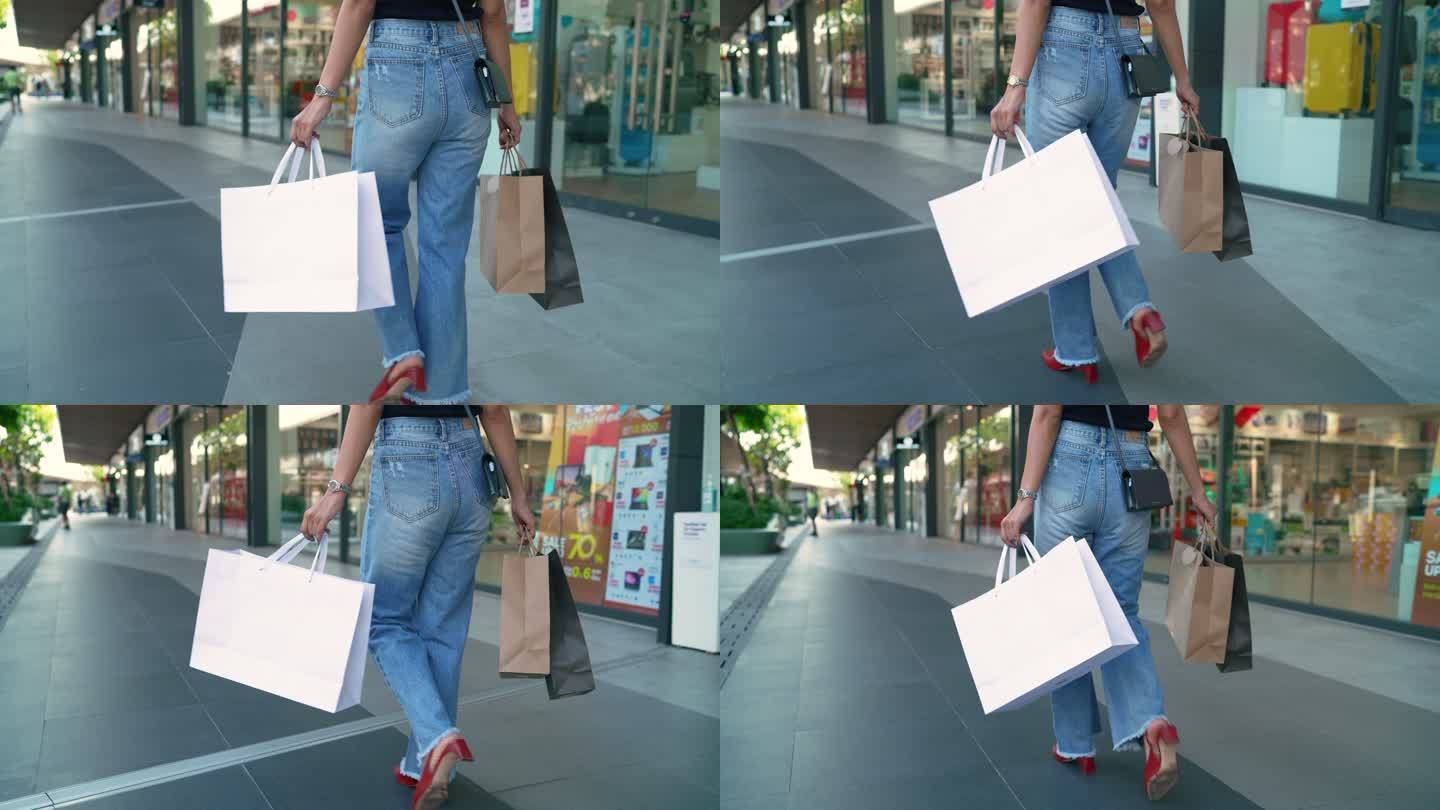 年轻的亚洲女性手拿着很多袋子在购物区行走。
