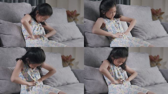 亚洲女孩因食物中毒而胃痛。她坐在家客厅的沙发上，用手捂住胃痛。一个女孩在吃快餐后身体受伤。
