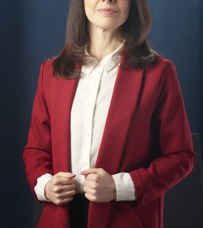 一位身穿红色夹克、头发乌黑的女士站在深蓝色背景上，在摄像机前摆姿势