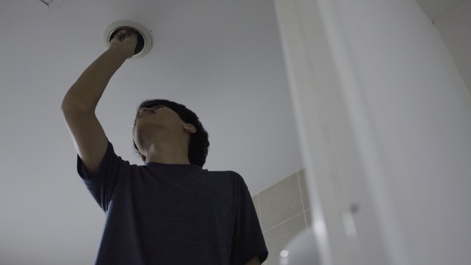 年轻的亚洲男人在家里用天花板上的新led灯泡更换紧凑型荧光灯灯泡