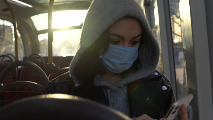 戴面具的女人在公交车上使用智能手机