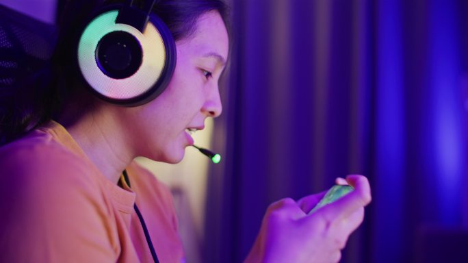 亚洲女性在家里的客厅里用智能手机数字小工具玩在线游戏