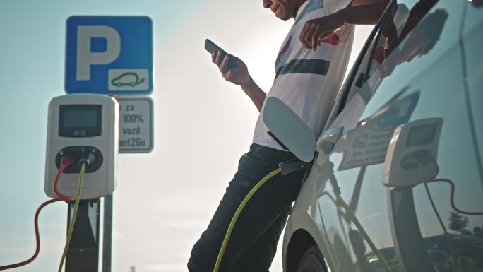 SLO MO年轻人在停车场充电时使用智能手机