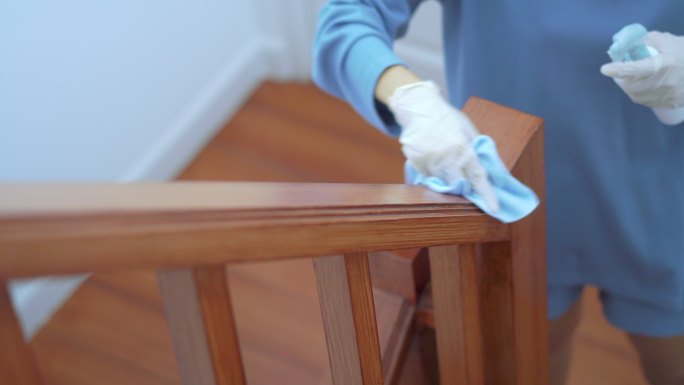 戴塑料手套的女性在楼梯栏杆上喷洒酒精消毒剂，对表面进行细菌或病毒消毒