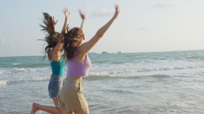 夏天，亚洲年轻漂亮的女性朋友在海滩上散步。迷人的两个女孩旅行者在热带海岛度假旅行时感到快乐和放松。