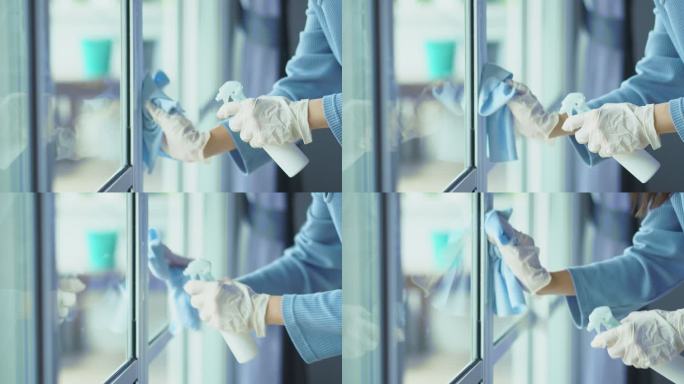 妇女戴着塑料手套，在玻璃门上喷洒酒精消毒剂，对表面进行细菌或病毒消毒