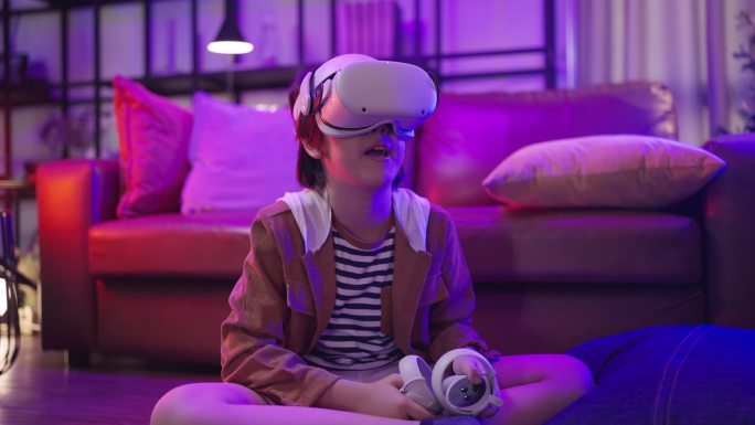 隔离期内，亚洲男童戴着VR或虚拟现实眼镜，戴着耳机站在家里的客厅里，在电视机前玩视频游戏，科技创新概