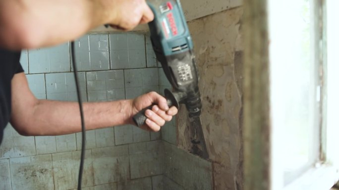 建筑商从浴室中移除旧瓷砖。拆除锤。