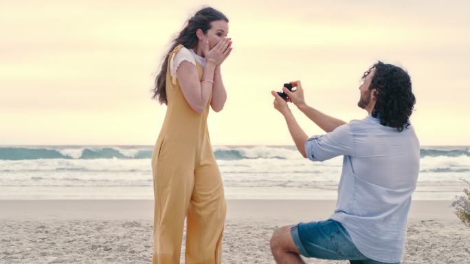 一对幸福的年轻夫妇在海滩求婚。一个年轻人向女友展示订婚戒指