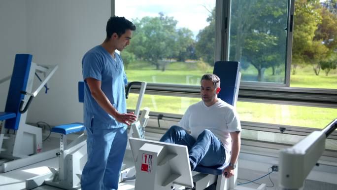 男性治疗师指导患者在物理康复中心的机器上锻炼双腿