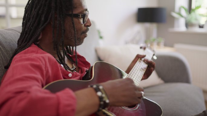 一个成年男子在家沙发上放松时弹吉他的4k视频片段
