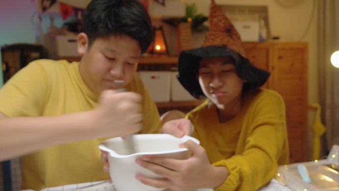 亚洲女孩戴着女巫帽，晚上和哥哥一起在家里做糖衣饼干，这是万圣节的生活方式理念。