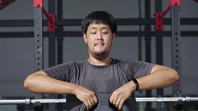 汗流浃背的亚洲男子举重杠铃板，瞄准肩部和背部