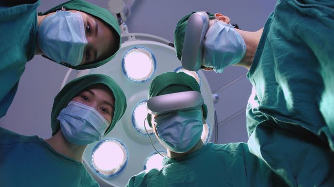 四名外科医生穿着防护服准备手术，他们戴着虚拟现实耳机，俯视手术灯背景上的摄像机。视角概念。
