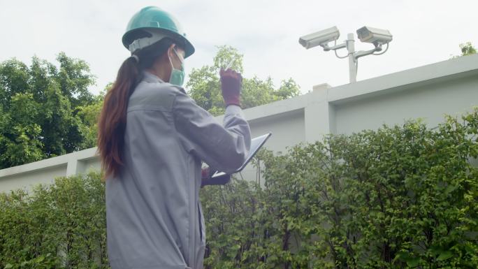 亚洲女性技术检查员检查大楼外的安全摄像头。工程师女性接触