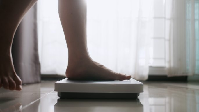 亚洲女性脚踩数字体重秤检查体重，称体重秤