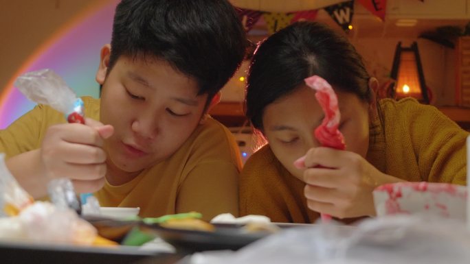 亚洲儿童在晚上一起在家里装饰糖霜饼干，这是万圣节的生活方式理念。
