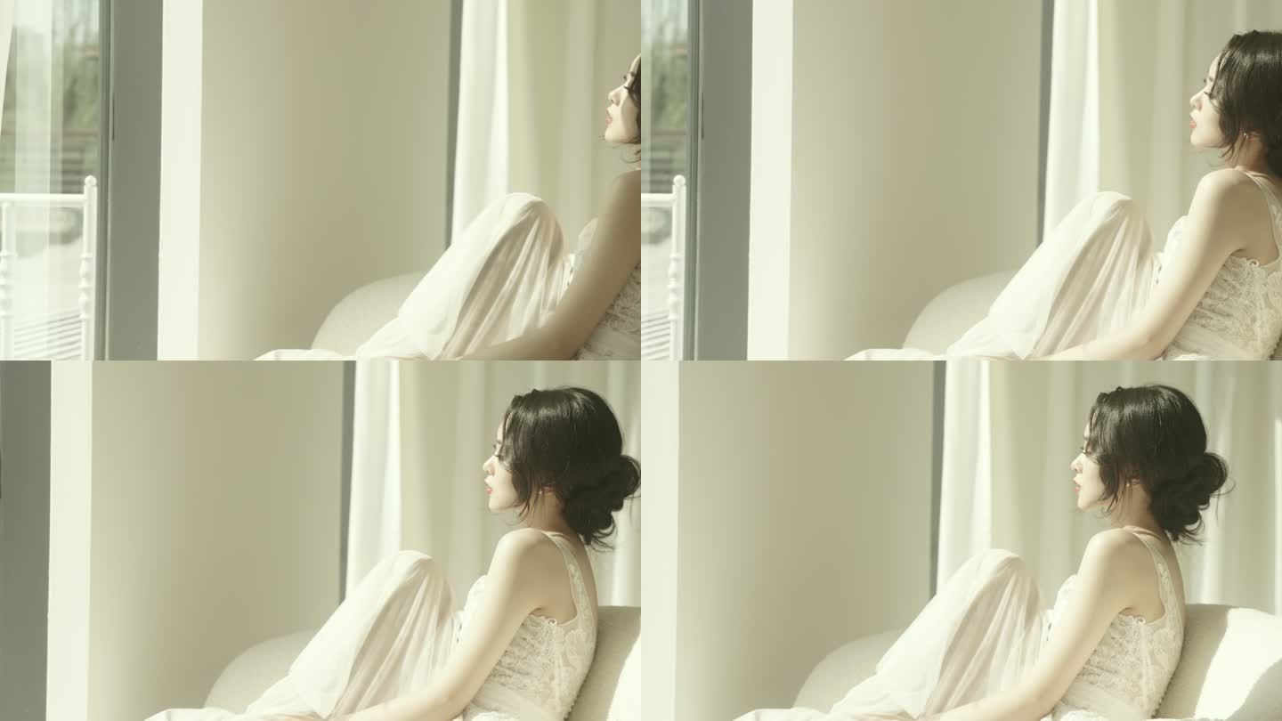 这位身着白色连衣裙的美丽亚洲新娘坐在落地窗前的沙发上慢镜头拍摄