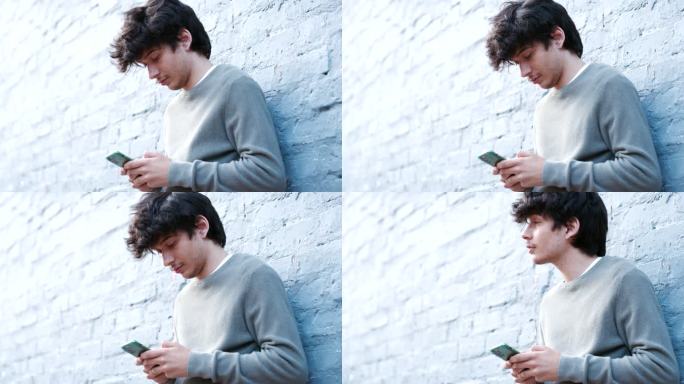 一个年轻人靠在灰色墙壁上使用智能手机的4k视频片段