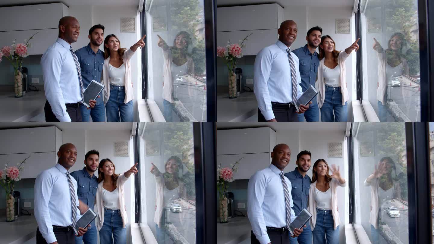 兴奋的夫妇和拿着平板电脑的房地产经纪人一起看着公寓的窗景
