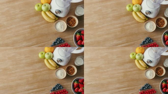 厨房台面上的搅拌机上方，周围是健康营养的配料。草莓、苹果、橙子、酸奶、坚果围着餐桌上的榨汁机。健康饮