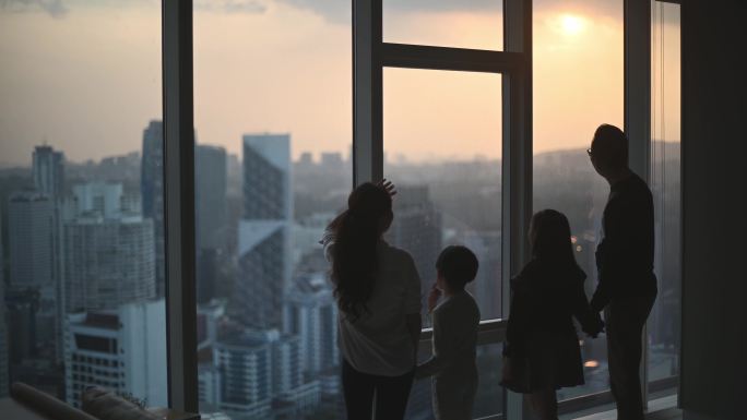 吉隆坡市亚裔华人家庭和两个孩子在起居室透过窗户欣赏美丽的日落