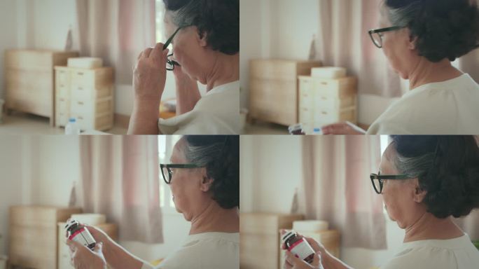 戴眼镜的老年妇女手持药瓶，在家里阅读药物标签并查看药物说明书的副作用。