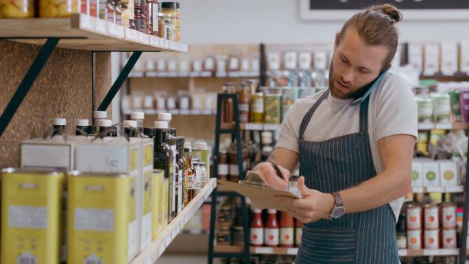 零售业工人在超市工作时与供应商通电话。男性跟单员或推销员，拿着剪贴板检查网上订单的库存，并在有机市场